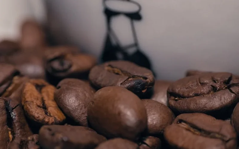 A rich espresso shot in a copper cup with steam rising, dark roast beans and hand-painted mug on a wooden counter.