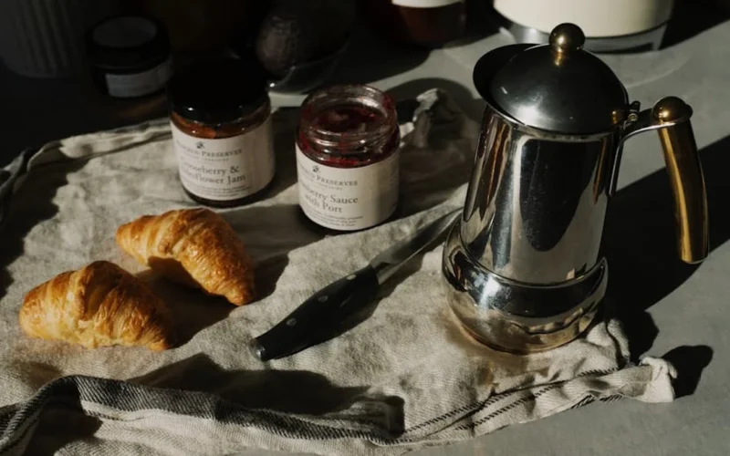 A traditional Finnish coffee table with pastries, sandwiches, and a steaming coffee cup under warm morning light.