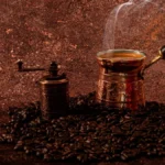 Dark roast coffee in a steaming cup next to a vintage roaster and notebook with temperature notes under warm lighting.