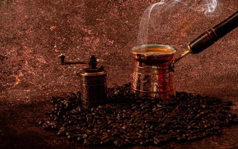 Dark roast coffee in a steaming cup next to a vintage roaster and notebook with temperature notes under warm lighting.
