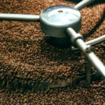 Dark roasted coffee beans steaming near a roasting machine under warm lighting.
