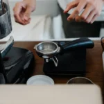 High-end espresso machine with 49mm puck in use, steam rising, warm lighting highlights polished surface.