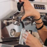 Barista steams milk to create flat white foam art in modern café setting.