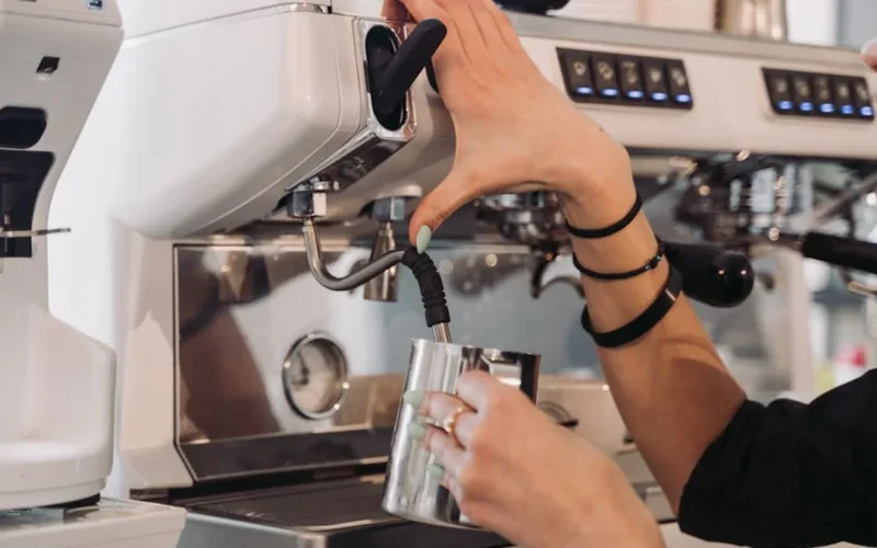 Barista steams milk to create flat white foam art in modern café setting.