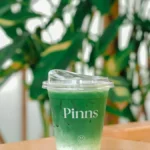 A vibrant matcha latte in a frosted glass with steamed milk foam in a modern café setting.