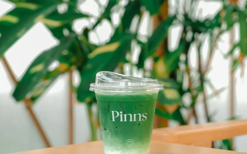 A vibrant matcha latte in a frosted glass with steamed milk foam in a modern café setting.