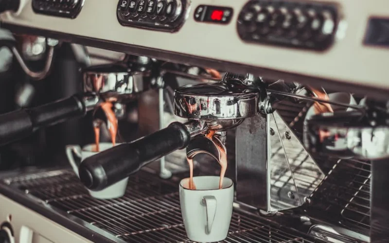 Dark coffee beans grinding into portafilter with espresso steaming from white cup