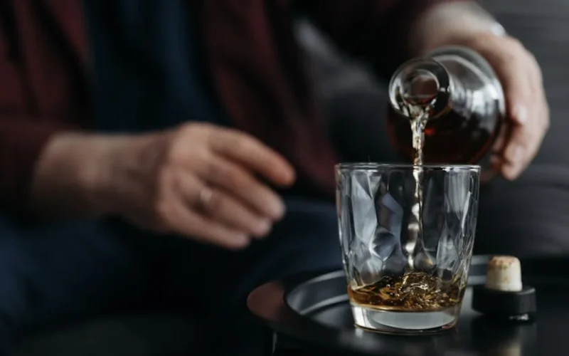 Harrison Ford pours Glenmorangie whiskey into a crystal glass at Sunset Tower with golden light reflecting off the liqui