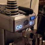Coffee grinder dispensing dark roast beans into burr grinder under golden lighting.