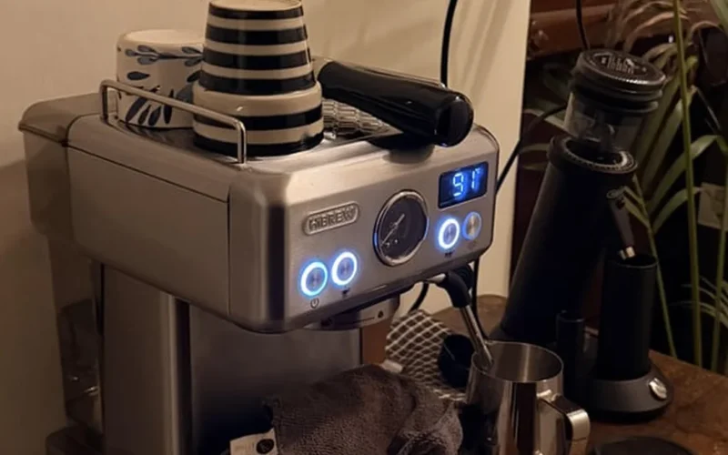Coffee grinder dispensing dark roast beans into burr grinder under golden lighting.