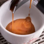 Close-up view of high-extraction coffee basket with flowing coffee liquid under studio lighting.