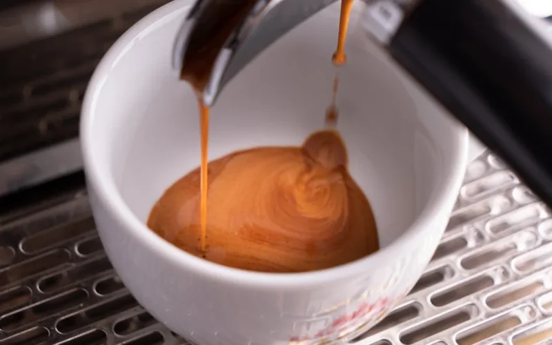 Close-up view of high-extraction coffee basket with flowing coffee liquid under studio lighting.