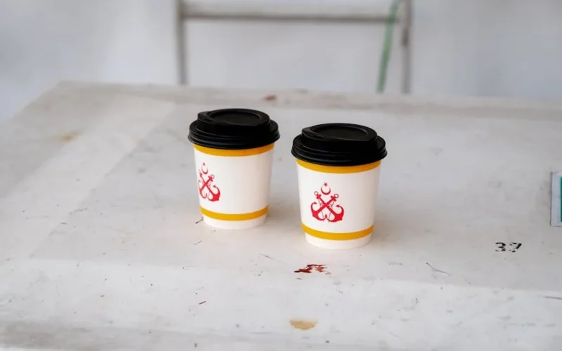 Pride flag placed on a coffee cup with steam rising and golden light reflecting on the surface.