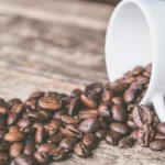 Roasted coffee beans spilling from two commercial coffee roasters onto a countertop under warm lighting.