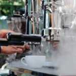 Glowing coffee roaster emitting steam with dark beans in rotating drum under warm lighting.
