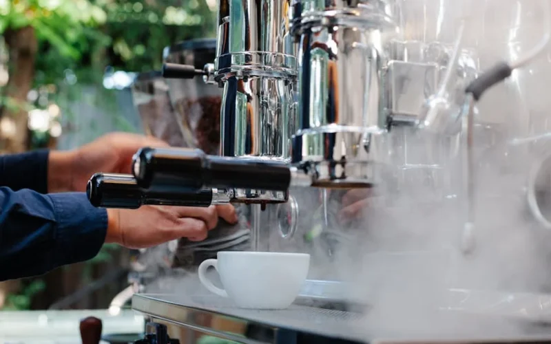 Glowing coffee roaster emitting steam with dark beans in rotating drum under warm lighting.