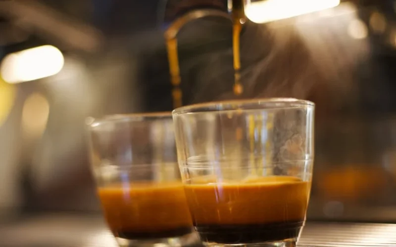 Artisan roasting coffee beans in high-end machine with steam and golden lighting.