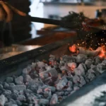 A roaster adjusts a temperature probe on a drum roaster in a steam-filled industrial kitchen.
