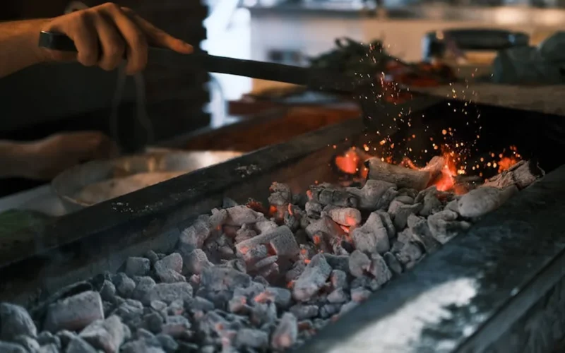 A roaster adjusts a temperature probe on a drum roaster in a steam-filled industrial kitchen.