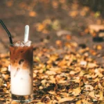 Iced coffee with milk and palm sugar syrup layers, tropical leaves in background.