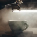 Brass coffee machine steaming milk into artistic froth on marble counter under warm lighting.