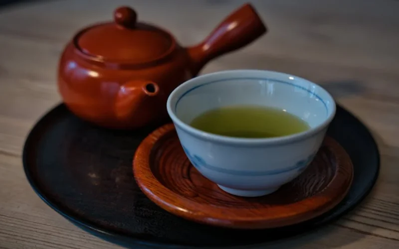 A steaming cup of puer tea on a bamboo tray with aged leaves and clay teapot under soft lighting.