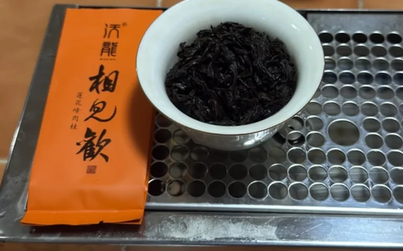 Ajar of dark, wiry tea leaves with charcoal roast aroma under golden light on a wooden table.