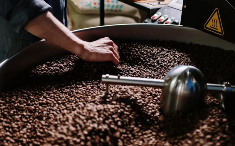 Coffee roaster in action with steam rising from beans during the roasting process.