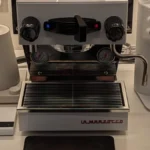 High-end coffee grinder in modern kitchen with light reflecting off its surface and coffee grounds in portafilter.