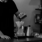 Binocular dripper brewing two coffee streams into separate cups with soft lighting and modern bar setup.