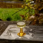 A glass of Matassa wine on a wooden table with fresh herbs under warm lighting.