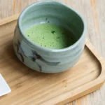 A steaming matcha bowl being whisked with a bamboo whisk in a traditional Japanese tea room.