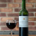 A dark merlot wine bottle on a wooden table with a glass of wine and a wine map notebook in natural light.