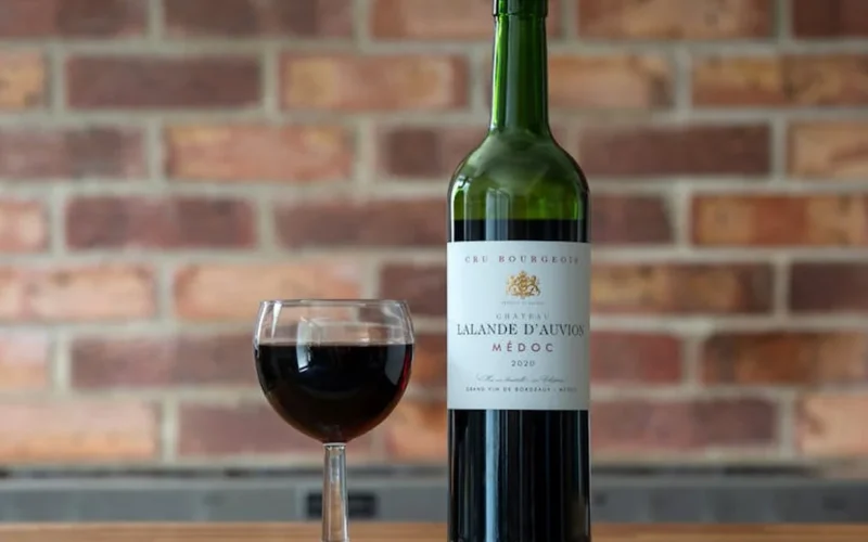 A dark merlot wine bottle on a wooden table with a glass of wine and a wine map notebook in natural light.