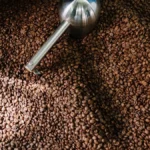 Hand-operated coffee roaster spinning green beans in a warm Mexican kitchen with steam rising.