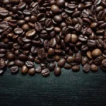 Coffee beans spilling from a wooden roaster with steam rising from a pour-over in a clay mug under golden light.