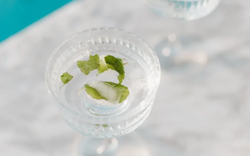 A glass jar with crushed mint and basil steeping in iced tea, surrounded by fresh herbs and a ceramic pitcher.