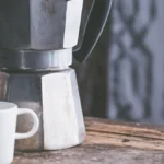 Moka pot brewing on wooden table with steam rising and board games nearby.
