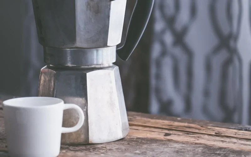 Moka pot brewing on wooden table with steam rising and board games nearby.