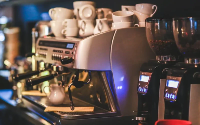 Modern dual-group coffee machine brewing with steam rising in a well-lit café setting.