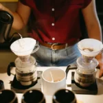 Baristas prepare pour-over coffee in a modern café with natural light and local art displayed on the walls.