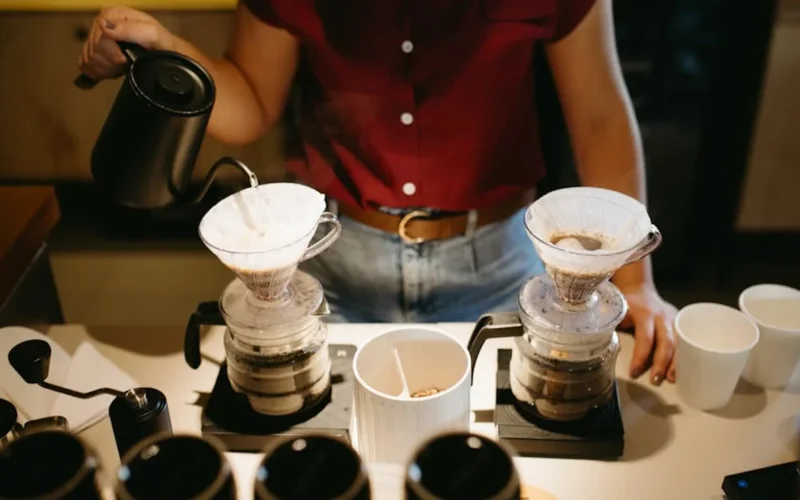 Baristas prepare pour-over coffee in a modern café with natural light and local art displayed on the walls.