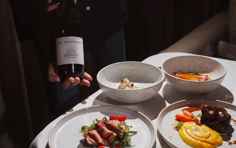 Chef plates wine reduction over vegetables at Paso Robles vineyard during sunset.
