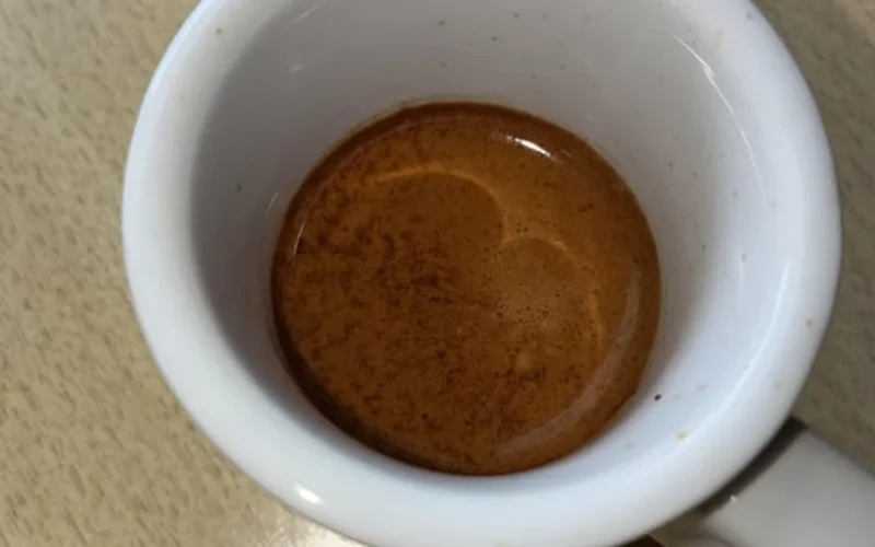 Dark roast coffee beans spilling into black cup with steam from espresso machine