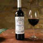 A dark wooden table features a Cabernet Franc wine bottle, glass of wine, and open notebook under warm lighting.
