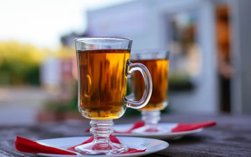 A steaming tea mug placed on a wooden table with dried tea leaves and a journal nearby.