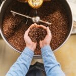 Dark roasted coffee beans spilling from a vintage roaster onto a marble countertop with steam rising nearby.
