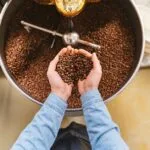 Dark roasted coffee beans spilling from a vintage roaster onto a marble countertop with steam rising nearby.