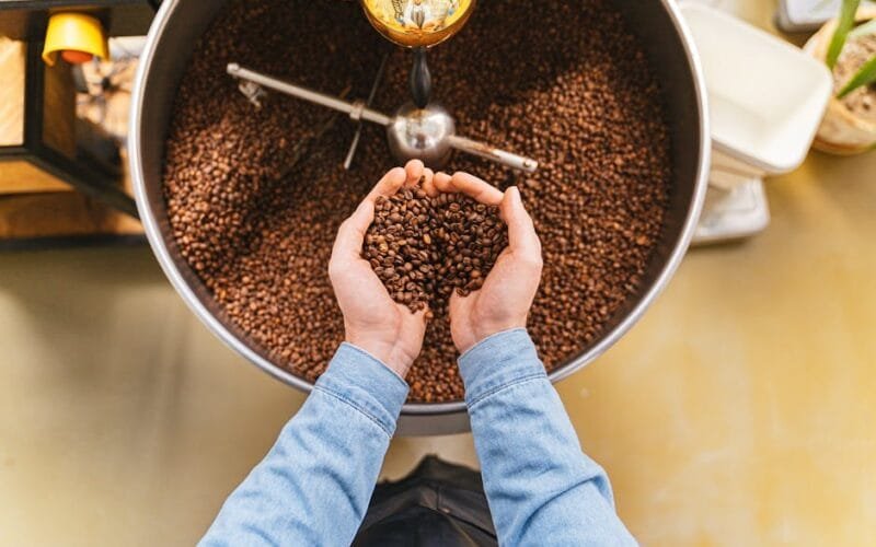 Dark roasted coffee beans spilling from a vintage roaster onto a marble countertop with steam rising nearby.