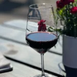 A glass of Pinot Noir on a wooden table with sunlight through a vineyard window.
